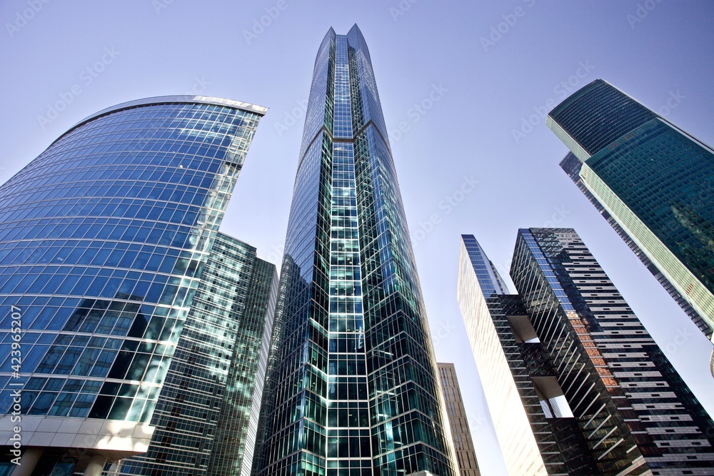 Modern office buildings against bright blue sky. Bottom-up view. Glass facades of skyscrapers with contrasting highlights and reflections. Economy development, finance and business concept. Downtown.