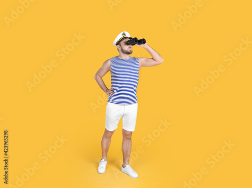 Young sailor with binoculars on yellow background