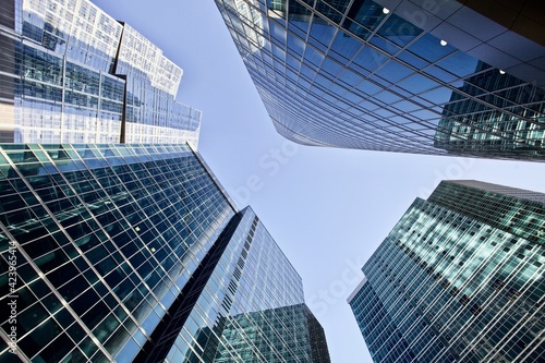 Modern office buildings against bright blue sky. Bottom-up view. Glass facades of skyscrapers with contrasting highlights and reflections. Economy development  finance and business concept. Downtown.