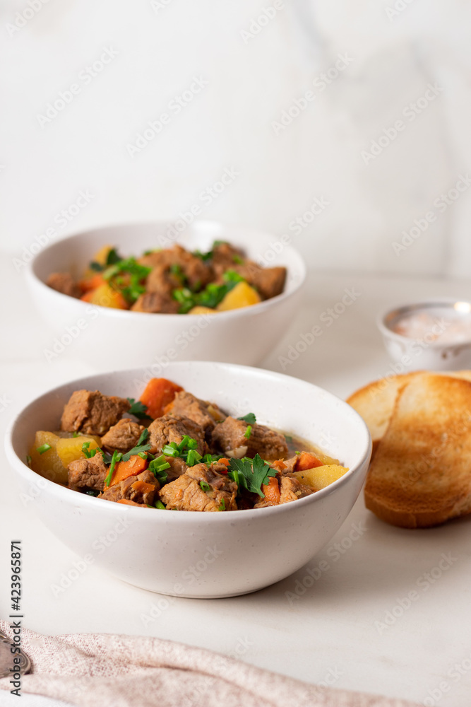 Goulash, beef stew with vegetables and thyme in a white plate with onion and greens. Goulash, beef stew with vegetables and thyme in a white plate with onion and greens.