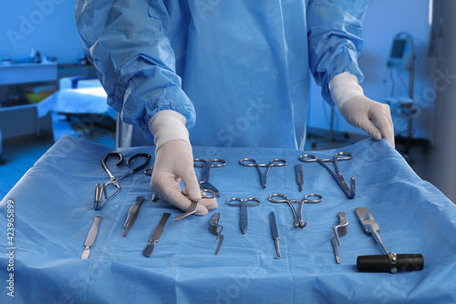 Nurse near table with different surgical instruments in operating room, closeup photo