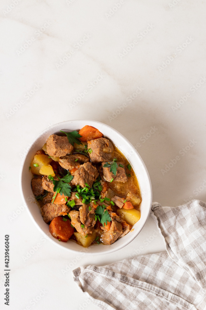 Goulash, beef stew with vegetables and thyme in a white plate with onion and greens. Goulash, beef stew with vegetables and thyme in a white plate with onion and greens.