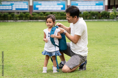 Asian father is helping to carry the schoolbag to daughter with happy moment after the school time, concept of parent care, education and back to school for student.