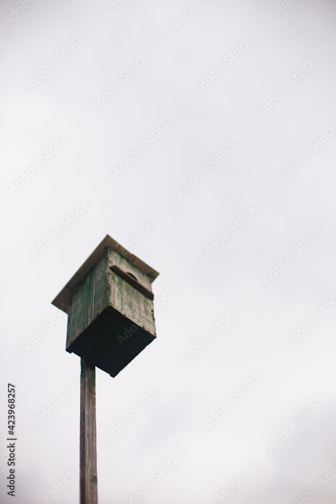 Old homemade wood birdhouse with peeling green paint in overcast sky