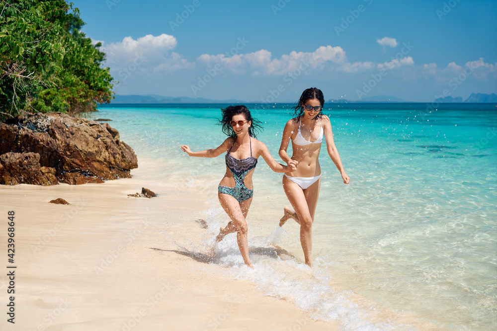 wo young women friends having fun and running on the tropical beach during summer vacation