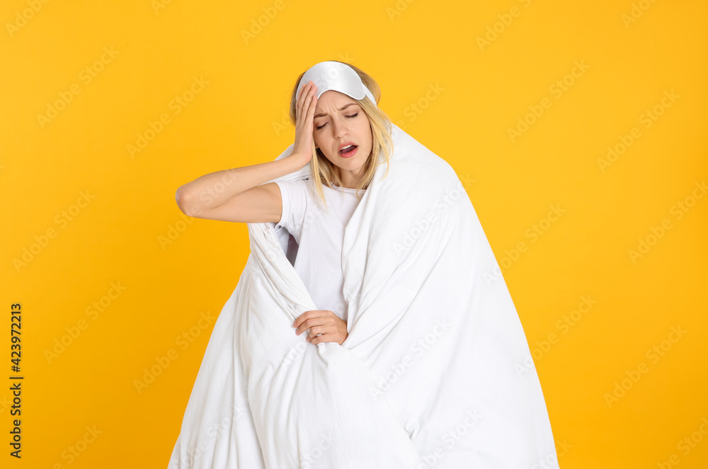 Young woman in sleeping mask wrapped with soft blanket yawning on yellow background Young woman in sleeping mask wrapped with soft blanket yawning on yellow background