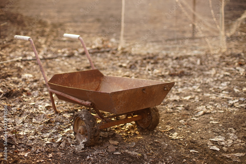Old rusty cart on wheels stands on the ground in the garden Old rusty cart on wheels stands on the ground in the garden