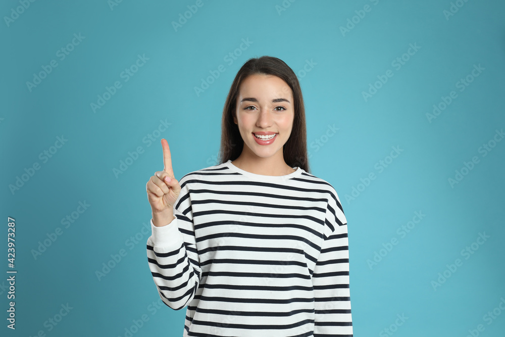 Woman showing number one with her hand on light blue background Woman showing number one with her hand on light blue background