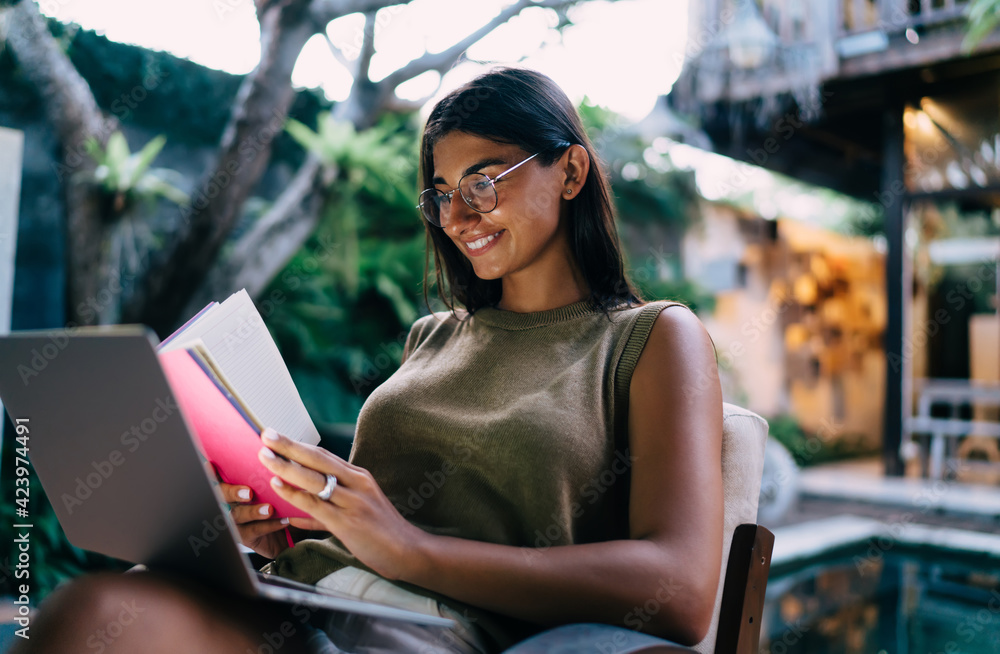 Gorgeous ethnic lady using netbook and reading diary while working remotely on terrace Gorgeous ethnic lady using netbook and reading diary while working remotely on terrace