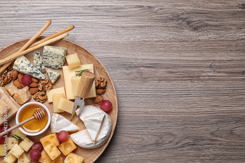 Cheese plate with honey, grapes and nuts on wooden table, top view. Space for text