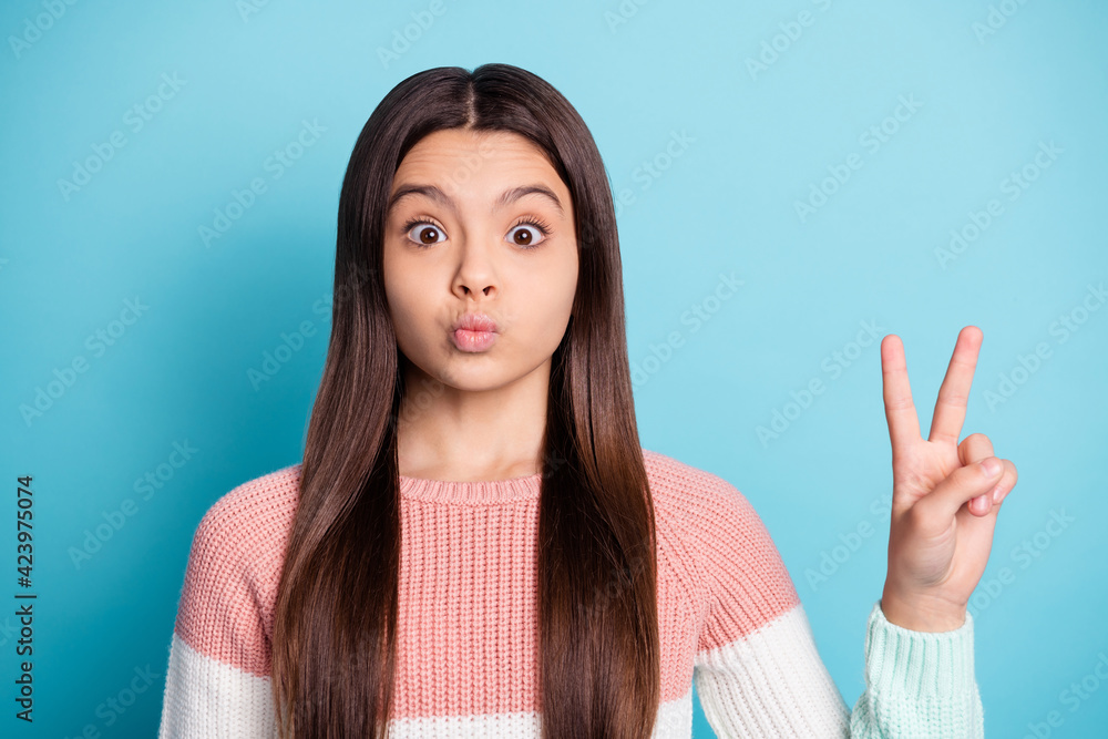 Photo of young schoolgirl pouted lips send air kiss show peace cool v-sign isolated over blue color background Photo of young schoolgirl pouted lips send air kiss show peace cool v-sign isolated over blue color background