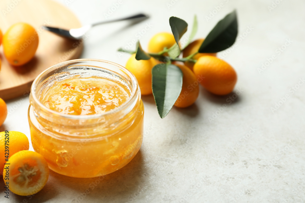 Delicious kumquat jam in jar and fresh fruits on light grey table, space for text Delicious kumquat jam in jar and fresh fruits on light grey table, space for text