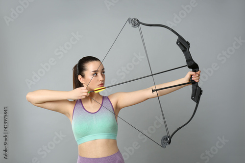 Young woman practicing archery on light grey background photo