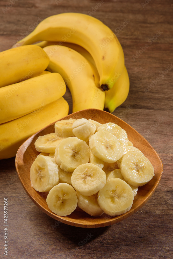 A banch of bananas and a sliced banana on wood background.