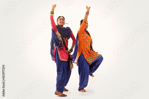 Two Giddha Dancers performing a dance step together with hands in the air. 