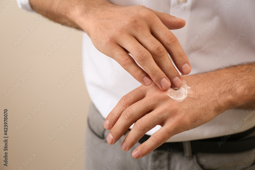 Man applying cream onto hand on beige background, closeup Man applying cream onto hand on beige background, closeup