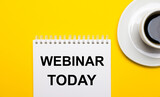 On a bright yellow background, a white cup with coffee and a white notepad with the words WEBINAR TODAY