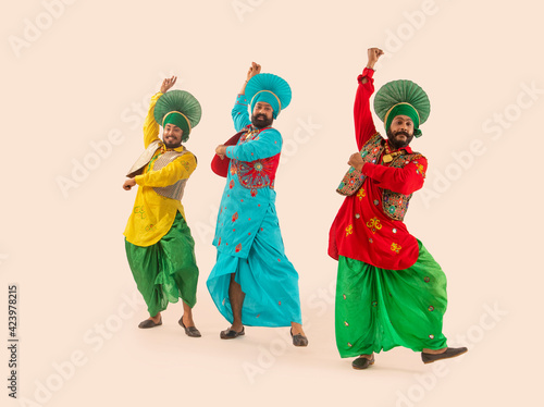 Three Bhangra dancers performing a dance step with hand gestures. 