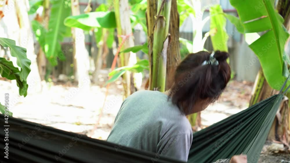 Young Asian woman happily sitting in a hammock swinging in the middle of a banana tree.