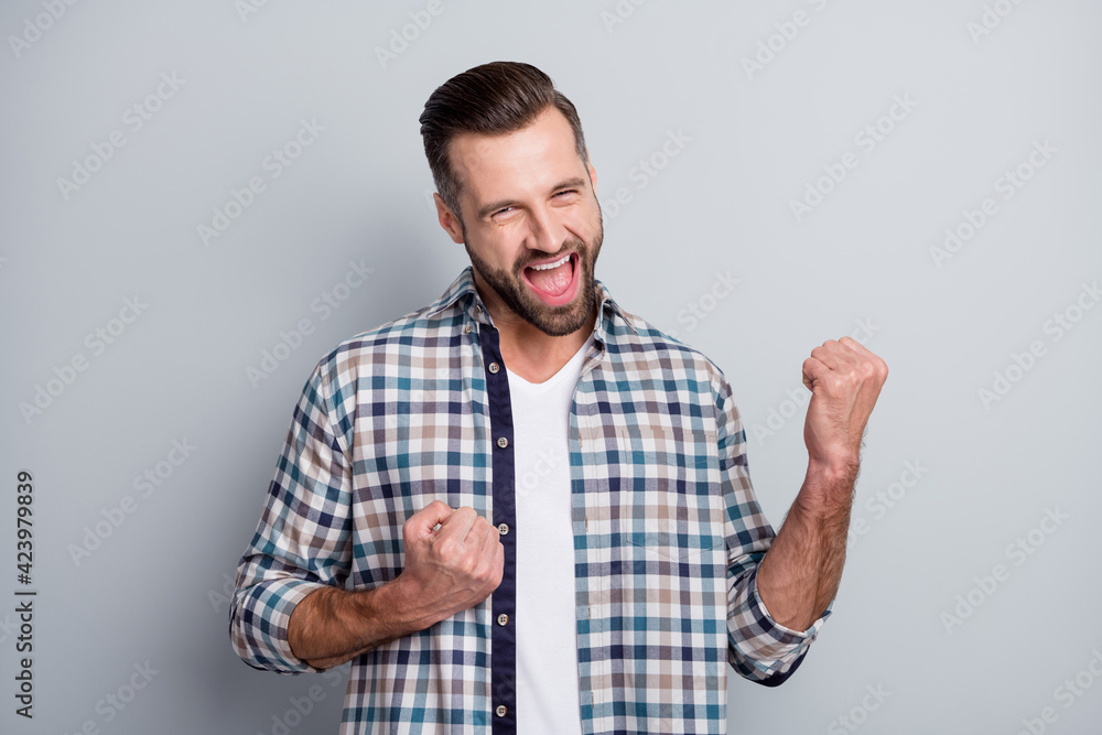 Photo of young attractive handsome crazy smiling positive excited man hold fists in victory isolated on grey color background Photo of young attractive handsome crazy smiling positive excited man hold fists in victory isolated on grey color background