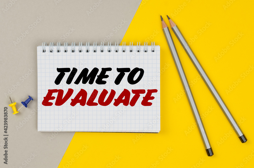 On a yellow-gray background are pencils, buttons and a notebook in which it is written - TIME TO EVALUATE On a yellow-gray background are pencils, buttons and a notebook in which it is written - TIME TO EVALUATE