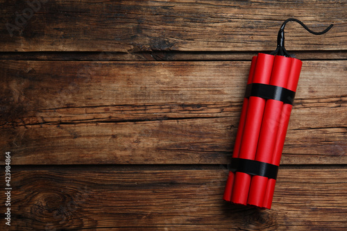 Red explosive dynamite bomb on wooden background, top view. Space for text photo