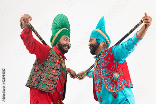 Two Bhangra Dancers standing with Khunda behind their neck. 