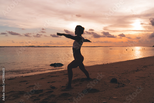 Slim female doing Warrior II pose on seashore