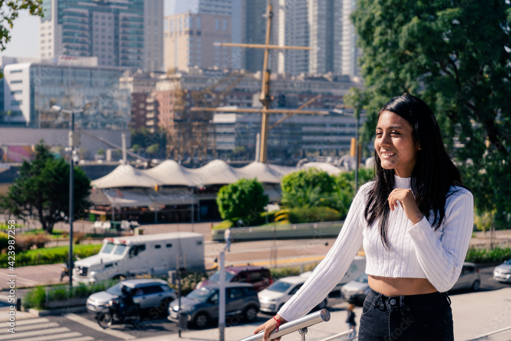Medium shot portrait of a smiling black haired Latina woman with the modern city in the background. writing space.