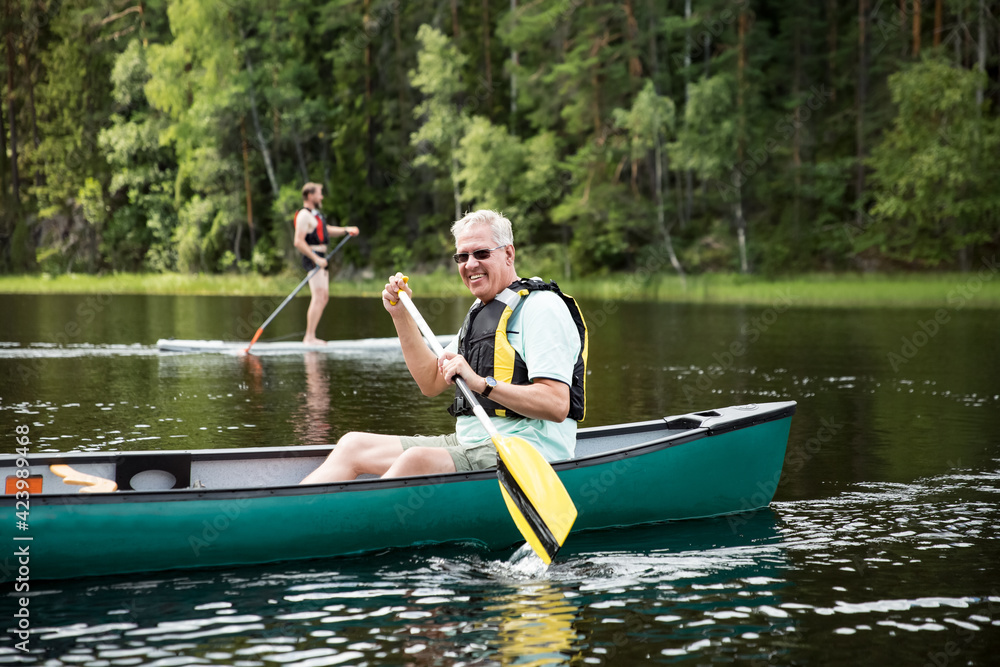 Happy mature couple in life vests canoeing in forest lake. Sunny summer day. Tourists traveling in Finland, having adventure. Happy mature couple in life vests canoeing in forest lake. Sunny summer day. Tourists traveling in Finland, having adventure.