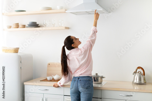 Smiling woman select mode on cooking hood in kitchen