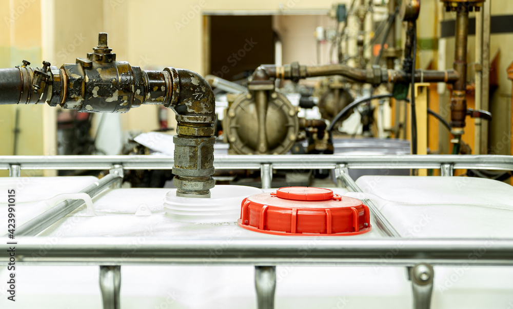 The large white tanks red lid of chemical open. Suction pipes for transferring to main storage tank inside of factory. The large white tanks red lid of chemical open. Suction pipes for transferring to main storage tank inside of factory.