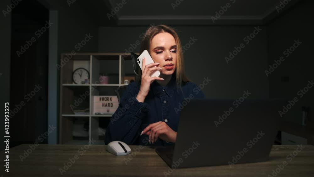 Attractive woman sitting at home at a table with a laptop and working remotely, looking at laptop screen and calling on the phone. Work online on the Internet. Attractive woman sitting at home at a table with a laptop and working remotely, looking at laptop screen and calling on the phone. Work online on the Internet.