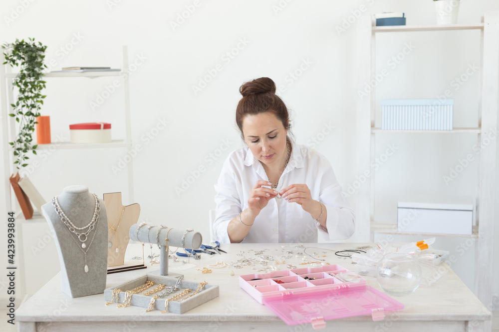 Beautiful young enthusiastic caucasian woman making beautiful unique costume jewelry while sitting at her work table. Concept of hobby and favorite work
