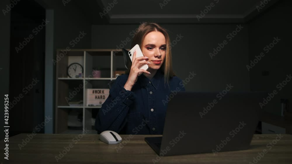 Positive woman sitting at home at a desk in a cozy room, working on a laptop and talking on the phone with a smile on his face. Positive woman sitting at home at a desk in a cozy room, working on a laptop and talking on the phone with a smile on his face.