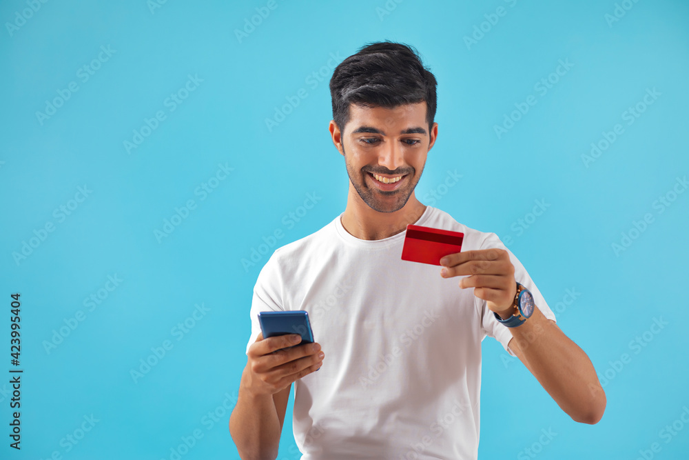 A young man placing an order with his credit card and mobile phone. 	