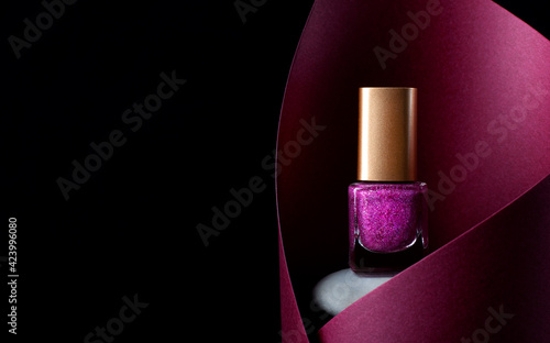 Nail polish of glittering pink color on stone inside the red paper cut against the black background. Copy space