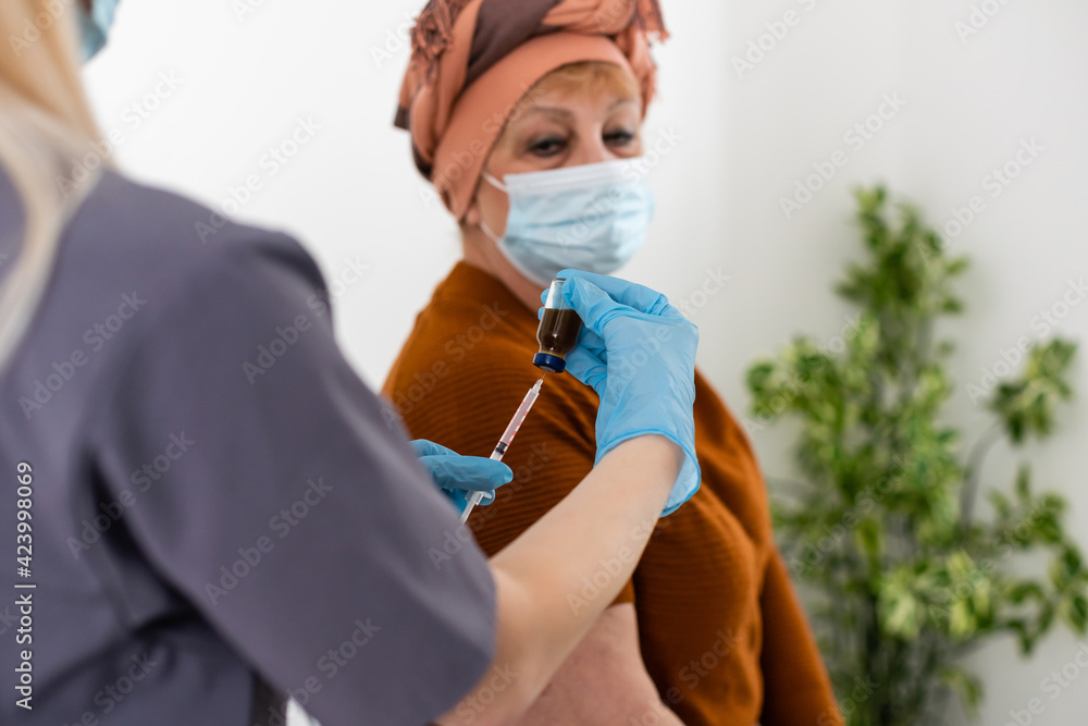 Naklejka premium cheerful young nurse giving a vaccine injection to elderly woman at home