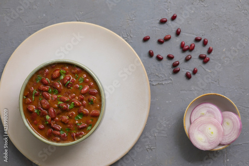 A PLATE WITH A BOWL OF RAJMA CURRY SERVED ALONG WITH RAW ONIONS	
