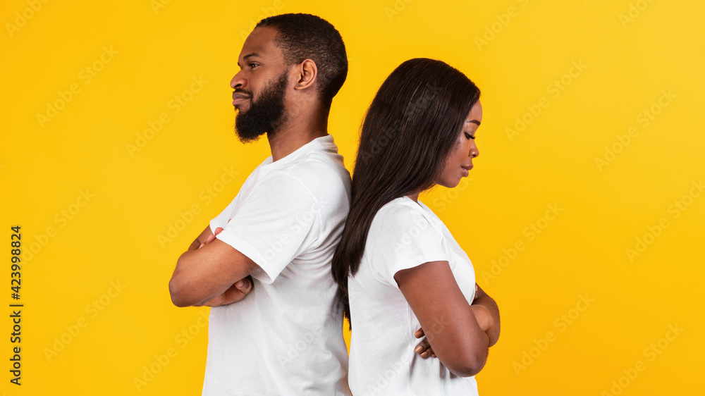 Black couple standing back to back, yellow studio wall Black couple standing back to back, yellow studio wall