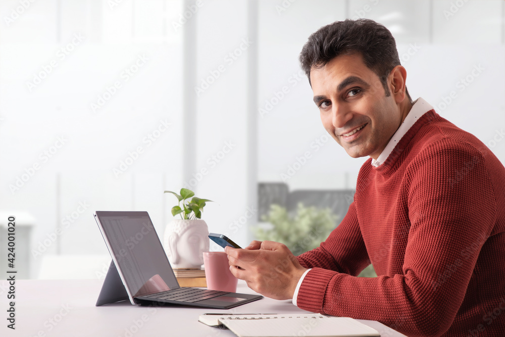 A CORPORATE PROFESSIONAL HAPPILY LOOKING AT CAMERA WHILE USING MOBILE PHONE A CORPORATE PROFESSIONAL HAPPILY LOOKING AT CAMERA WHILE USING MOBILE PHONE