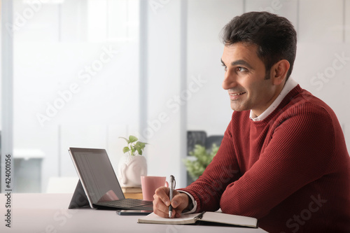 A CORPORATE EMPLOYEE SITTING AND LOOKING ABOVE WHILE HAPPILY WRITING DOWN ON NOTEPAD 