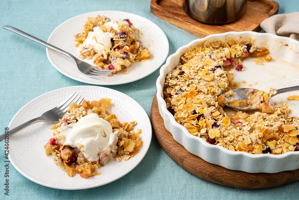 Two plate with apple and pear crumble with ice cream, streusel. Sweet dessert with stewed fruit topped crisp crumbly mixture served ice cream. Apple cobbler pie in baking dish on tablecloth. Side view Two plate with apple and pear crumble with ice cream, streusel. Sweet dessert with stewed fruit topped crisp crumbly mixture served ice cream. Apple cobbler pie in baking dish on tablecloth. Side view