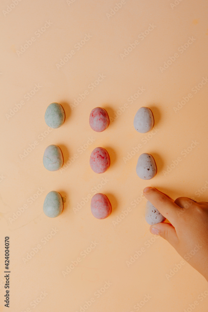 Children's hand holding a small colorful chocolate Easter egg on an orange background. Small chocolate eggs. Traditional Easter sweet. Copy Space.