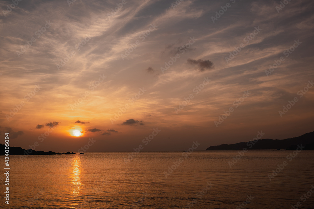 Beautiful seascape at sunset. Sun setting behind a mountain and sea with calm water movement.