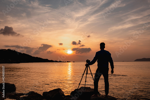 Silhouette of photographer preparing equipment to take a photo at the sunset on the sea while using drone.