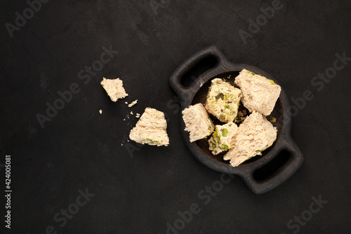 Sesame halva with pistachios on wooden serving platter, top view. Dark textured background, copy space. Middle eastern delicious plant-based sweets