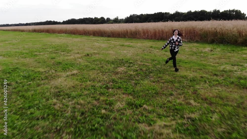 Aerial shooting of a cute young girl with long hair running in a meadow against a background of a yellow wheat field on a summer day Aerial shooting of a cute young girl with long hair running in a meadow against a background of a yellow wheat field on a summer day