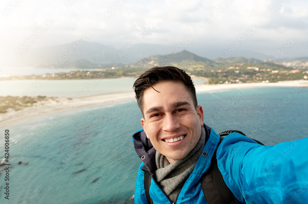 Young smiling man take a selfie photo of beautiful seascape panorama of Porto Giunco beach in Sardinia, Italy.