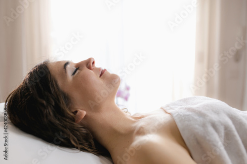 Side view attractive woman lying on spa bed with closed eyes and smile. White background in beauty center.